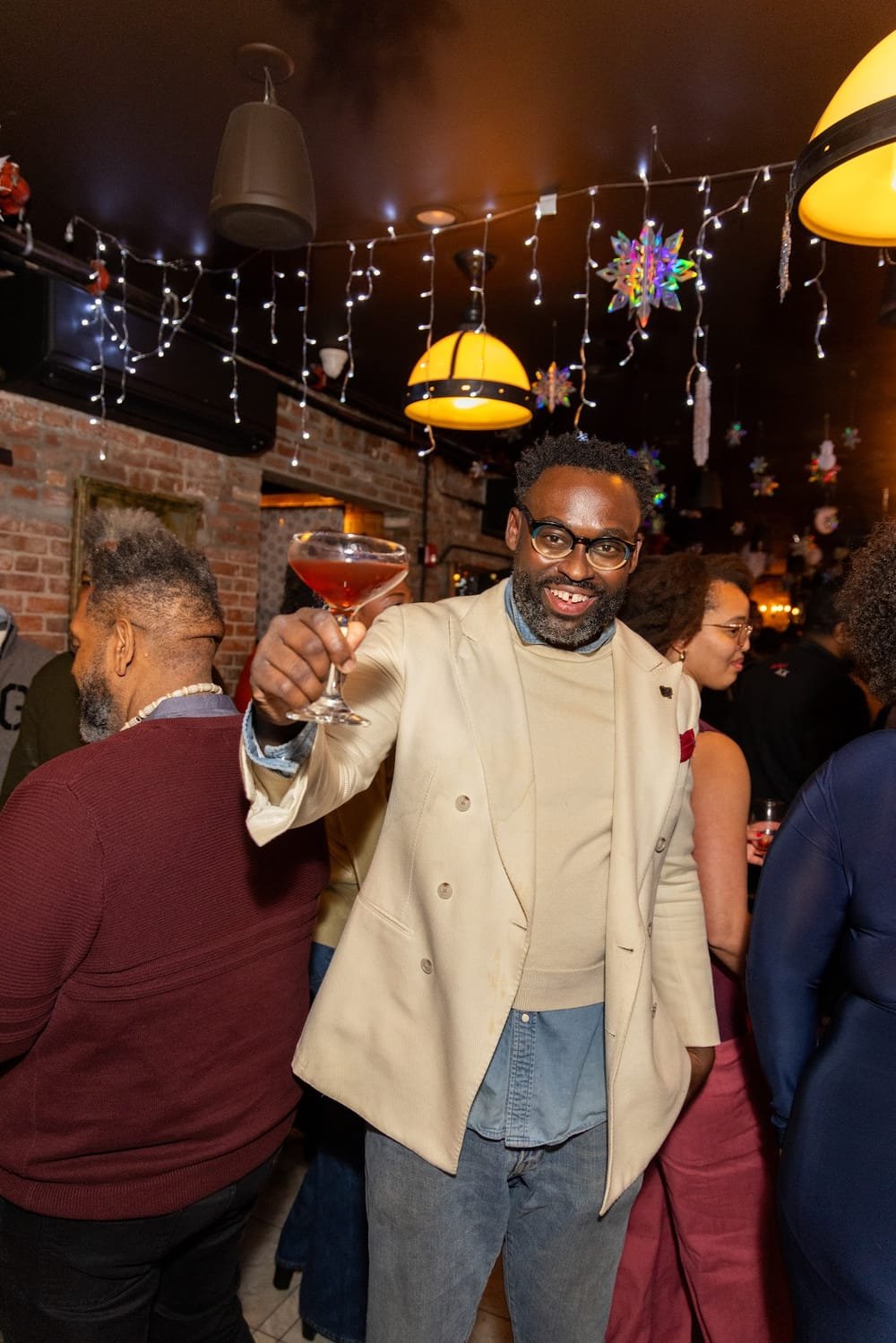 Jeff Lindor, founder of Gentlemen's Factory, raising a cocktail under the holiday lights at the 2025 Holiday Party at SAINT