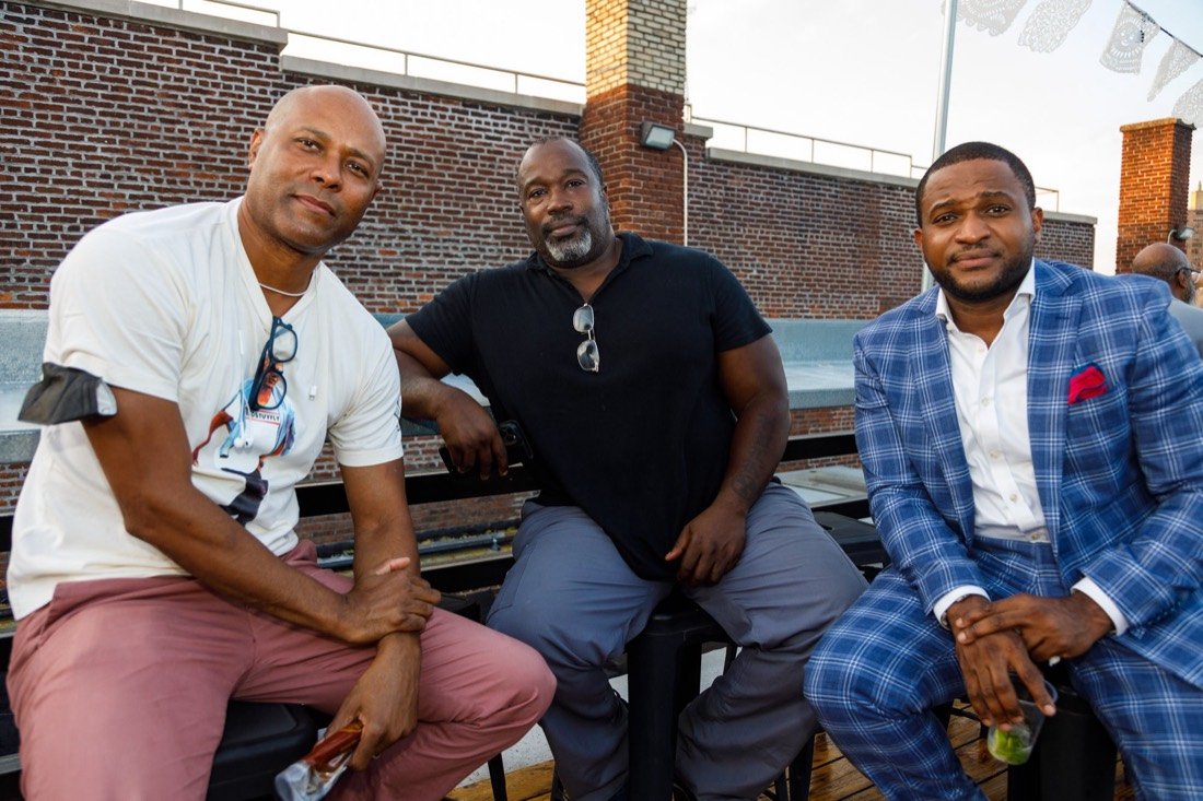 Three Gentlemen's Factory members seated together on a rooftop